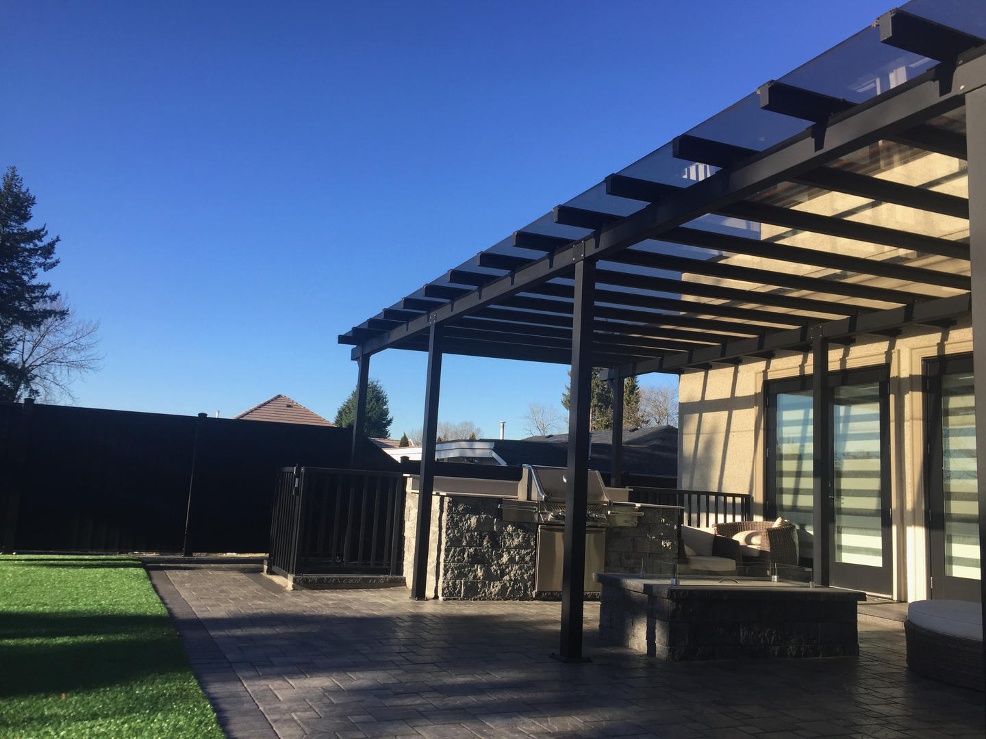 A patio cover with dark tinted glass with matching black aluminum beams