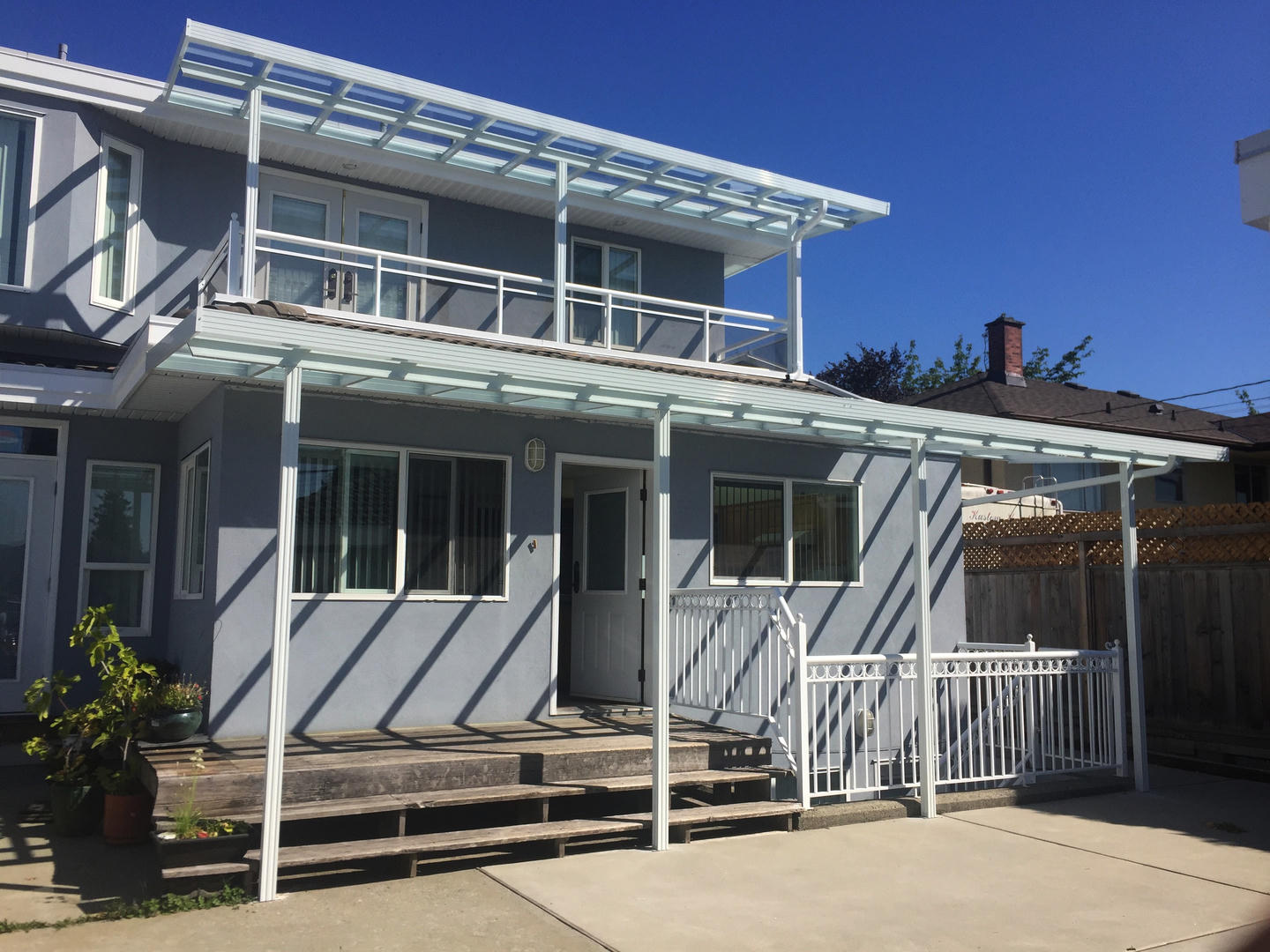 A pair of white aluminum/glass patio covers in a tiered layout across two storeys